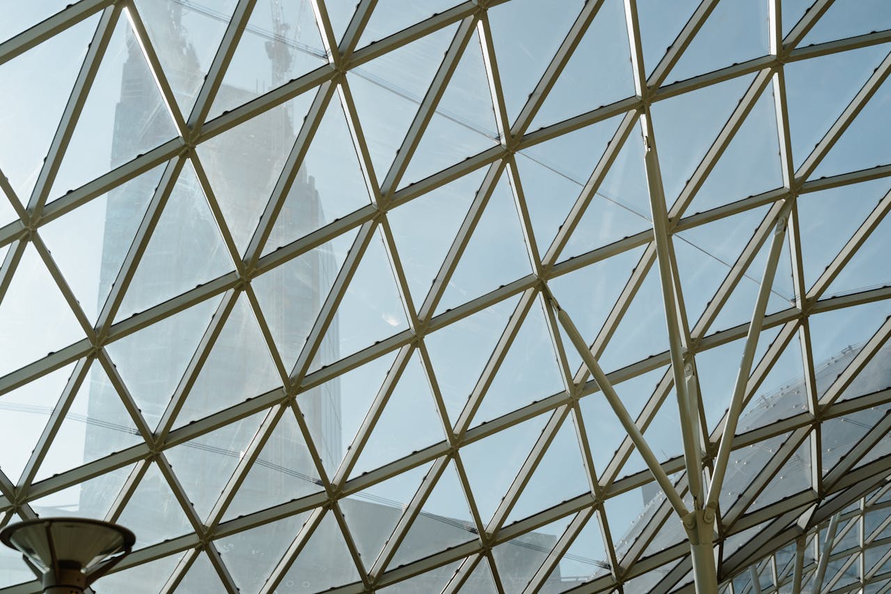 Architectural detail of a glass roof with geometric patterns and distant skyscraper view.