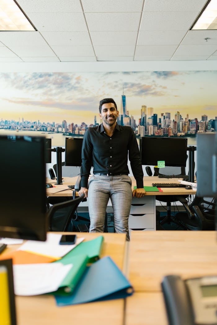 Confident man posing in a contemporary office setting with city skyline backdrop.